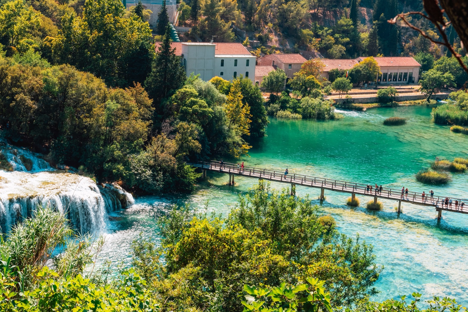 A wooden footbridge crossing turquoise water below a waterfall in Krka National Park