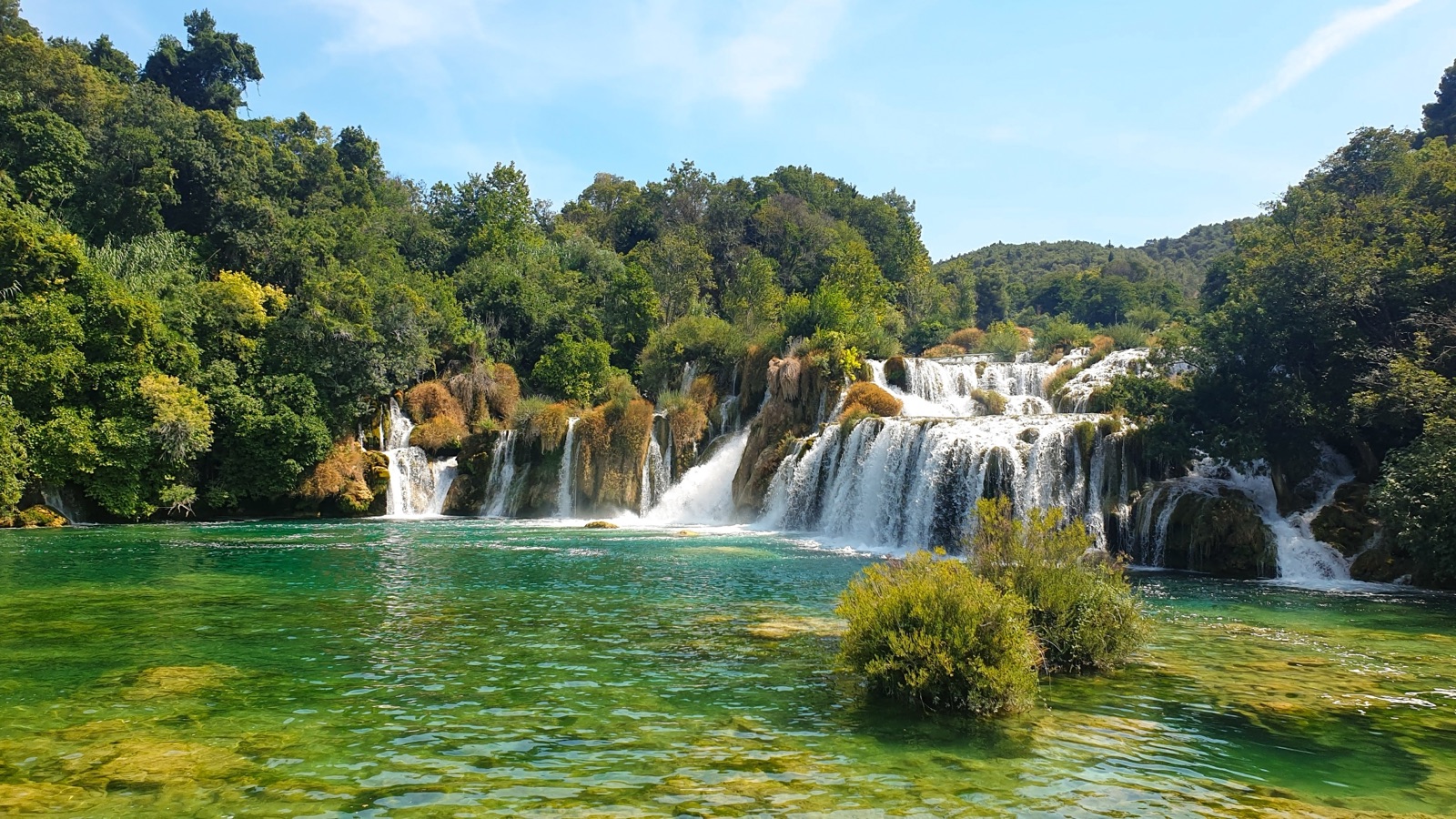 The wide cascades of Skradinski buk spilling over mossy travertine into a clear green pool, below wooded hills